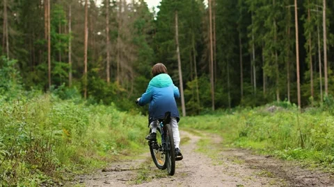 4K slow motion of a little boy riding a bicycle on a forest path from behind. Stock Footage 344880632