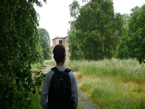4K slow motion of a man walking towards overgrown buildings Stock Footage 70319917