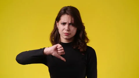 4k slow motion video of one girl showing thumb down on yellow background. C Stock Footage 229674262