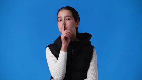 4k slow motion video of one girl looks around and showing silence sign over blue Stock Footage 235004127