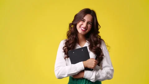 4k slow motion video of smiling girl holding a note book over yellow background. Stock Footage 231244307