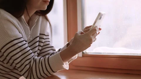 4K slow motion video of a young woman using a smartphone near a window at hom Stock Footage 327678204