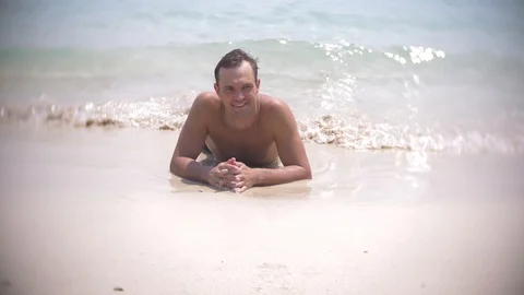 4k, slow motion, young man lies on white sand looking at camera and smiling Stock Footage 86666747