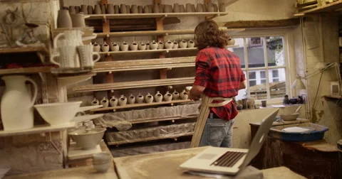 4K Small business owner in pottery studio looking at computer & checking sales Stock Footage