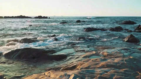 4K small ocean waves crushing into the rocks, orange sunset reflected over Stock Footage 153697881