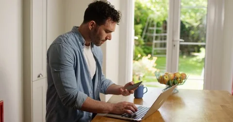 4K Smiling casual man making friendly phone call while working on laptop at home Stock Footage 80091630