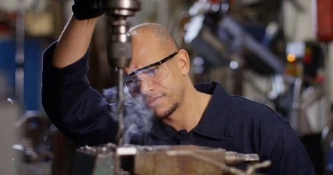 4K Smiling metal worker watching as large smoking drill bores into metal part Stock Footage 103858896