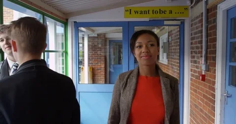 4K Smiling teacher walking through school building &amp; greeting some of her pupils Stock Footage 76952406