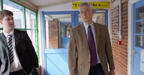 4K Stern school head master walking through building keeping an eye on students Stock Footage 76955827
