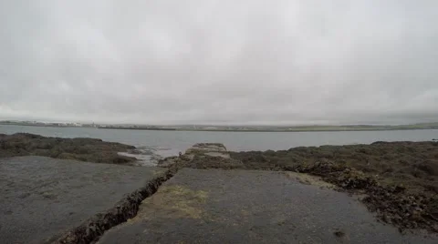 4K stone pier going out in the sea with seaweed all around it, grey clouded sky Stockbeeldmateriaal 47268967