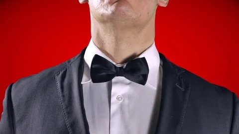 4K Stylish Man Using Hands to Fix Bow Tie, Red Background Tuxedo Black Suit Stock Footage 72335425