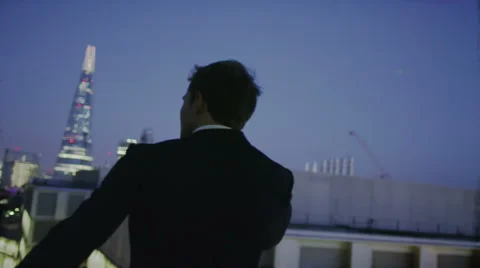 4K Successful businessman with cell phone looks out over London skyline at night Stock Footage