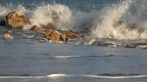 4k sunrise or sunset static shot of waves crashing on a rocks by a sandy beach Stock Footage 123469793