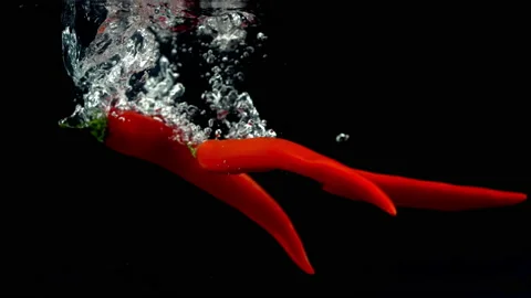 4K Super Slow-Mo Of Chilli Peppers Splash In Water Tank On Black Background Stock Footage 151391490