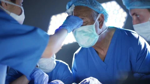 4K Surgeons operating on patient assistant wipes sweat from surgeon's face Stock Footage 63082808