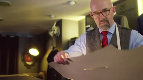 4K Tailor working in his shop, drawing templates on a piece of fabric Stock Footage 63230158