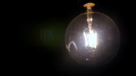 4K three filament light bulb swinging against a black background, globe retro Stock Footage 89185828