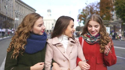   4k. Three young attractive women girlfriends walk in city street with smile.   Stockbeeldmateriaal 107071553