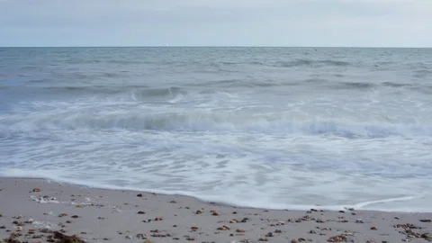4K timelapse of waves on pebble beach in Dorset, sail boats in background Stockbeeldmateriaal 95811076