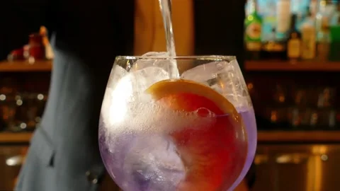 4K Tonic Poured Into Purple Gin Glass With Ice And Fruit Stock Footage