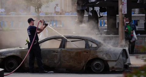 4K TRACKING SHOT OF FIRE FIGHTER PUTTING OUT A SMOLDERING CAR DURING PROTEST Stock Footage 131458009