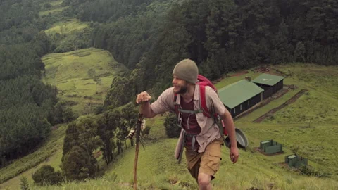 4k trekker walking away from log cabin to go hiking in green mountain range with Video stock 199620384