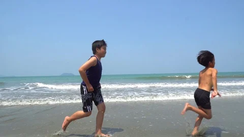 4k two Asian boy running on a beach with far ocean and blue sky. Stock Footage 87738039