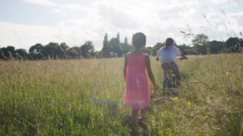 4K Two children run and cycle through a long grass meadow, in slow motion Stock-Footage 64742706