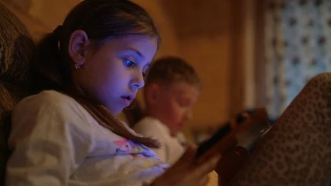 4K two children sitting immersed in gadgets with light from screens on face Stock Footage 107401447