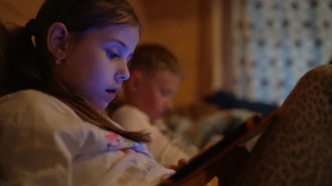 4K two children sitting immersed in electronic gadgets with light from screens o Stock-Footage 113705074