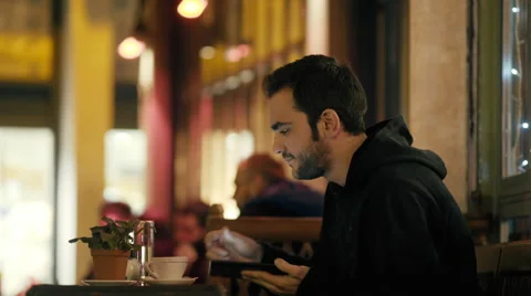 4K UHD Young man sitting in night cafe/bistro browsing tablet drinking coffee Stock Footage 58715524