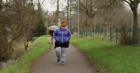 4K Unhappy overweight woman in leisure wear walking alone outdoors in the park. Stock Footage
