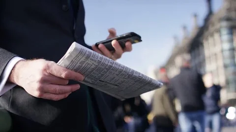 4K Unseen business man using his phone to check  financial data from a newspaper 69233973