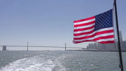 4K US Flag Waving San Francisco Oakland Bay Bridge And Waterfront Stock Footage 334461186