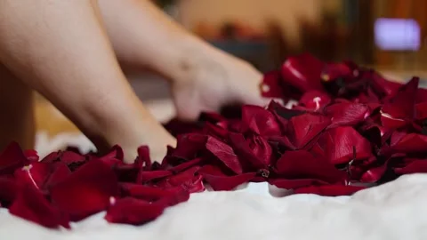 4K video close up. 60 fps. Bare female smooth shaved legs kick red rose petals Stock Footage 326825703