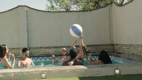 4K video of a group of friends playing with a ball in a swimming pool Stock Footage 220234394