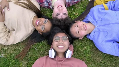 4k video of teens lying on grass with heads in circle looking at camera. Stock Footage 220257251