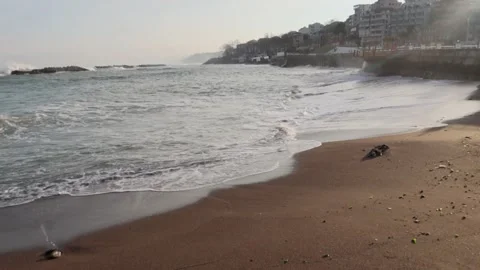 4K video of waves reaching a sandy beach with a coastal town view. Stock Footage 323002713