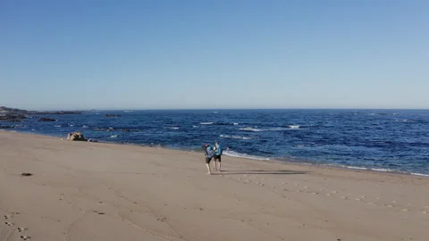 4K view of couple walking by wide sandy beach washed by Atlantic Ocean waves in Stock Footage 329742561