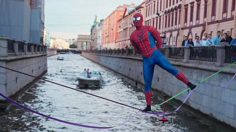 4k view of a street performer dressed as Spider-Man walking over river Stock Footage 343182700
