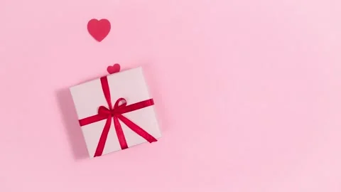4K White Gift Box Red Satin Ribbon and Decorative Hearts Pink Background Stock Footage 334444254