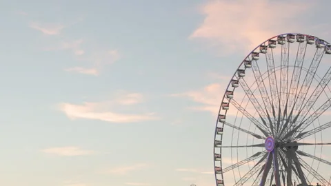 4K wide-angle shot of a giant Ferris wheel spinning gracefully against a pastel  Stock Footage 338174171