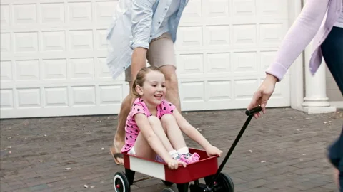 4k wide shot of mother pulling daughter in wagon as father guides daughter for t Stock Footage 201095600