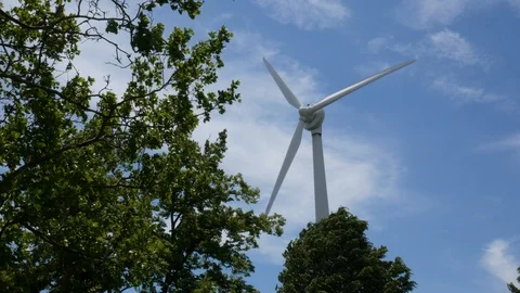4k wind turbine next to trees agianst blue sky Stock Footage 90861526