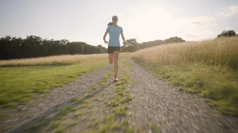 4K woman running fast behind camera in back light summer rural landscape Vídeos de archivo