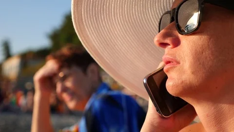 4K woman in white wide-brimmed hat and sunglasses on the beach using her phone Stock Footage