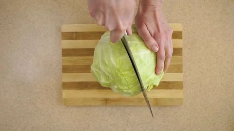 4K.  Woman’s hands are cutting the cabbage into two parts on a kitchen board Stock Footage 128329109