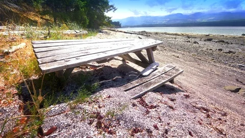 4K Wooden Picnic Beach Table, Rock Sand Beach Forest Background and Low Tide Video stock 80430519
