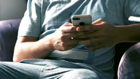 4k - A young adult sitting at home and scrolling through his phone. Stock Footage
