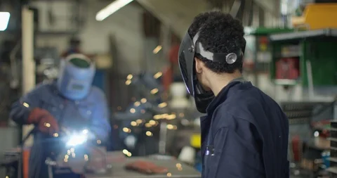 4K Young apprentice welder lifting visor &amp; smiling at camera in workshop Stock Footage 111661757
